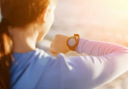 Auf dem Bild ist die Rückansicht einer Person zu sehen, die auf ihre Smartwatch schaut. Die Szene ist in warmes Sonnenlicht getaucht, was auf eine Outdoor-Aktivität hinweist.