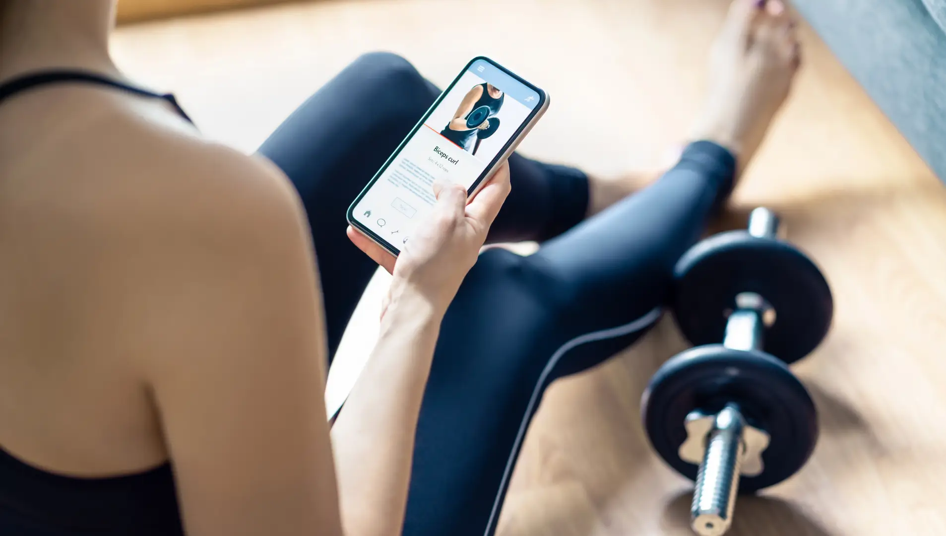 Eine junge Frau in Sportkleidung schaut sich Sportübungen auf ihrem Smartphone an.