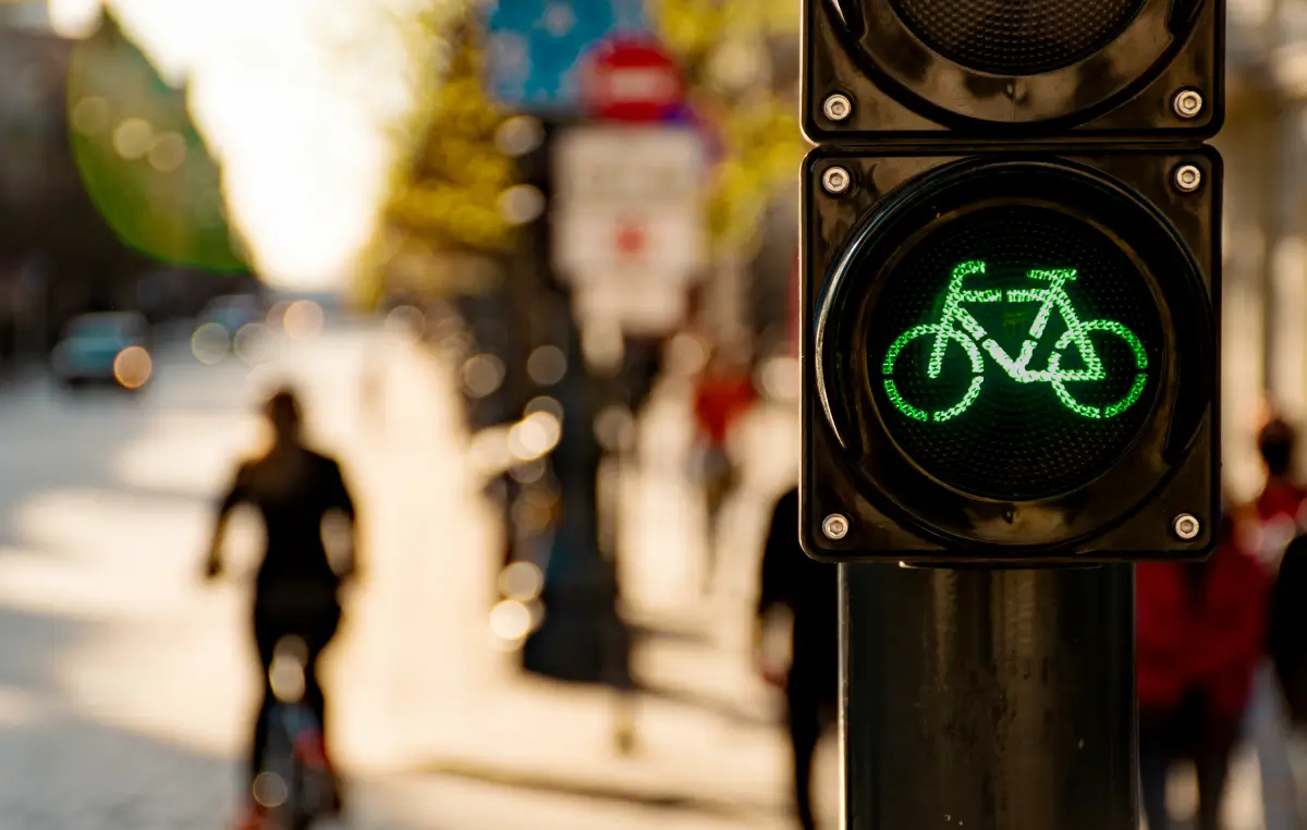 Das Bild zeigt eine grüne Ampel mit einem Fahrrad-Symbol, die Radfahrern das Überqueren einer Straße in einer städtischen Umgebung erlaubt.
