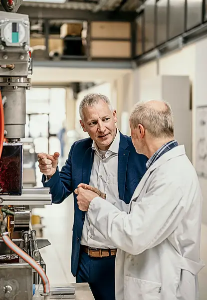 Zwei Personen führen eine angeregte Diskussion neben einer industriellen Maschine in einem technischen Umfeld.