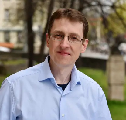 Das Bild zeigt Professor Carsten Könke mit Brille und hellem Hemd, der draußen steht und in die Kamera lächelt.