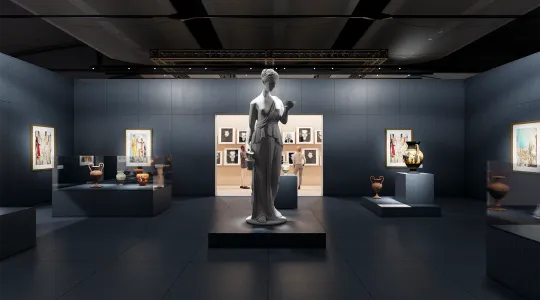 Ein Raum mit einer klassischen Skulptur im Vordergrund. An den Wänden sind Gemälde und Fotografien ausgestellt. Vitrinen mit antiken Vasen und Artefakten sind ebenfalls zu sehen. Im Hintergrund betrachten zwei Personen die ausgestellten Werke.