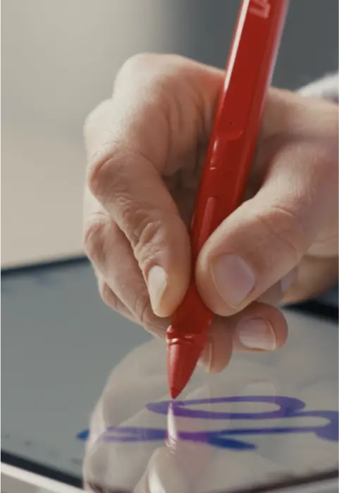 Eine Hand hält einen roten digitalen Stift und zeichnet eine blaue Linie auf einem Tablet.