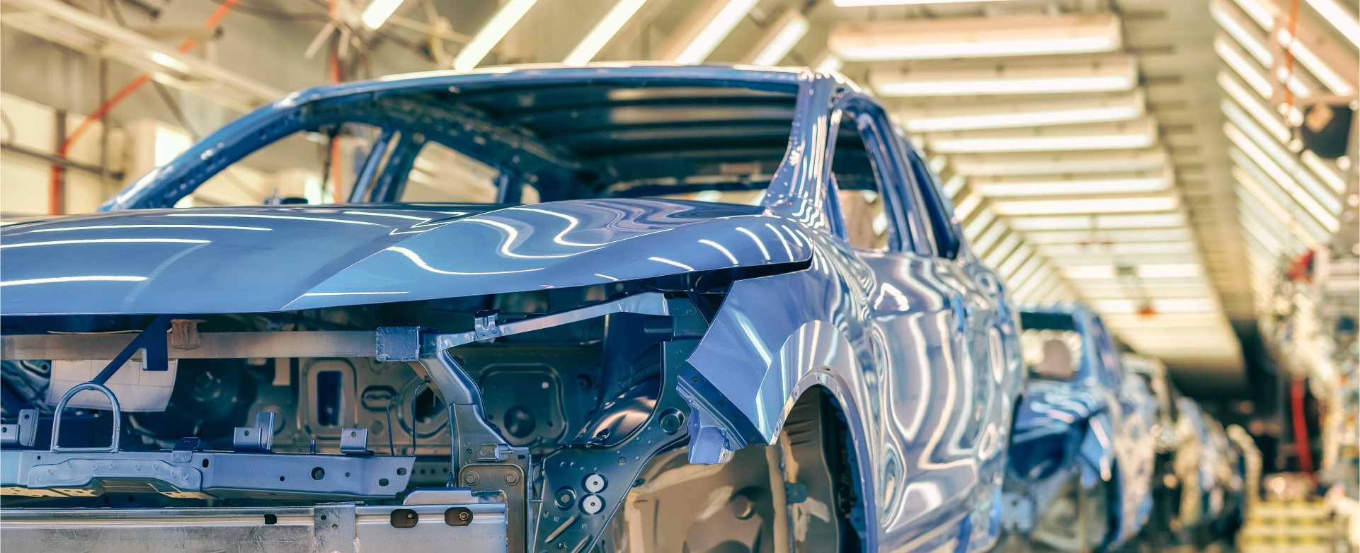 Eine blaue Auto-Karosserie bewegt sich durch eine Produktionslinie in einer hell beleuchteten Fabrikhalle.