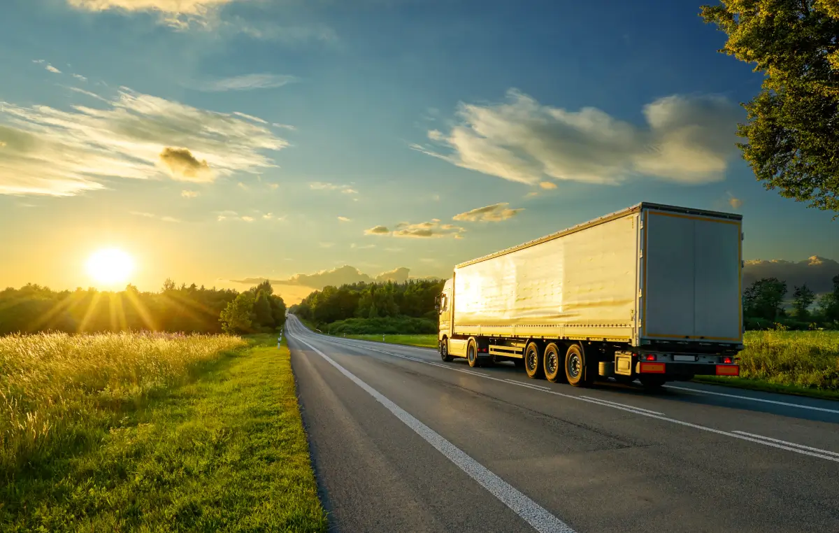 Ein Lastwagen fährt bei Sonnenuntergang auf einer Landstraße durch eine grüne Landschaft.