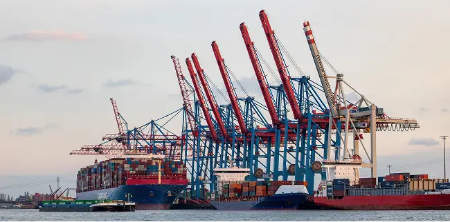 Große Container-Schiffe liegen im Hafen vor mehreren Verladekränen.