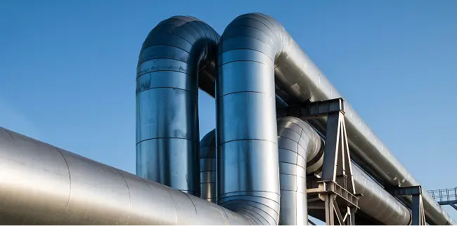 Mehrere große, silberne Industrie-Rohre verlaufen nebeneinander und über eine Stahlkonstruktion.