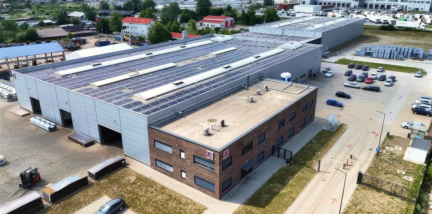 Luftaufnahme eines großen Industriegebäudes mit Parkplatz und umliegenden Gebäuden.