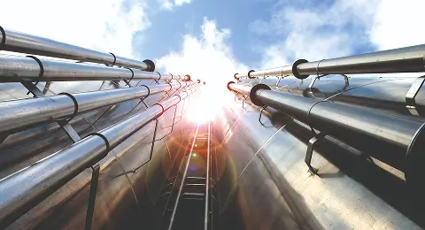 Blick nach oben auf mehrere große, glänzende Rohre mit Sonnenlicht im Hintergrund.