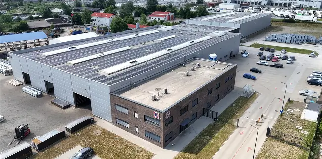 Luftaufnahme eines großen Industriegebäudes mit Parkplatz und umliegenden Gebäuden.