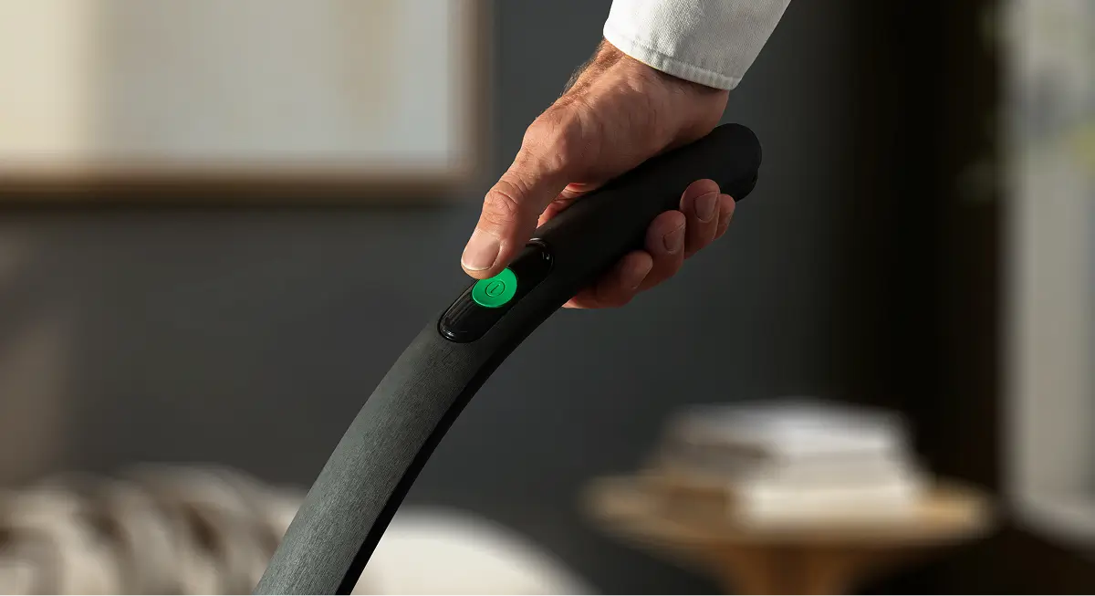 Eine Hand betätigt die grüne Einschalttaste an einem Staubsaugergriff.