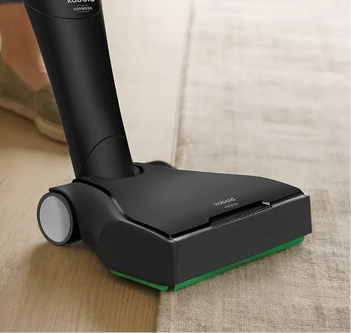 Eine Staubsaugerbürste fährt von einem Holzboden auf einen Teppich über.