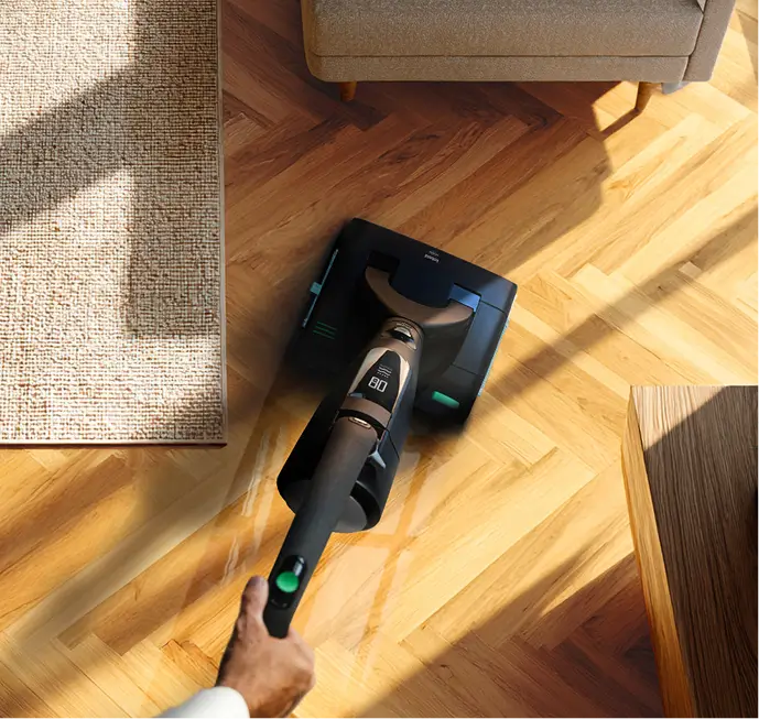 Ein Staubsauger saugt einen Parkettboden neben einem Teppich in einem Wohnzimmer.