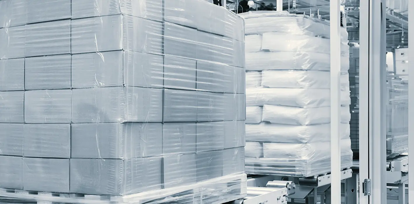 Paletten mit Kartons und Säcken, die in Folie verpackt sind, in einer Lagerhalle.