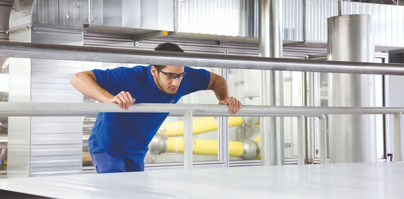 Arbeiter in blauer Kleidung beugt sich über ein Geländer in einer Produktionshalle.