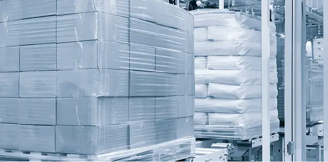 Paletten mit Kartons und Säcken, die in Folie verpackt sind, in einer Lagerhalle.