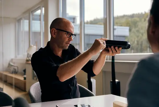 Eine Person hält ein schwarzes Haushaltsgerät in den Händen und demonstriert dessen Funktion.