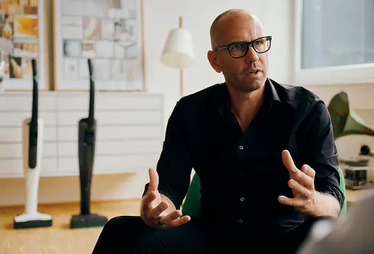 Eine Person sitzt im Gespräch, im Hintergrund stehen zwei kabellose Staubsauger.