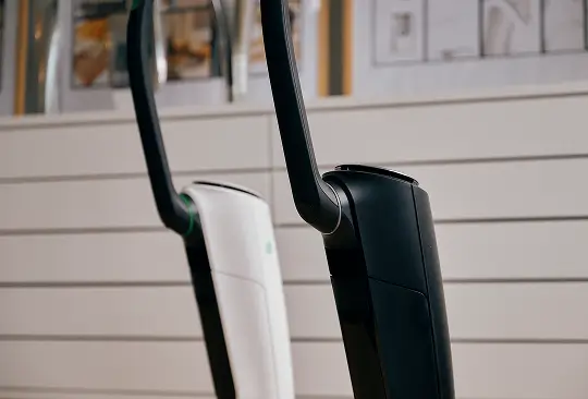 Zwei kabellose Staubsauger, einer weiß und einer schwarz, stehen nebeneinander vor einer Kommode.