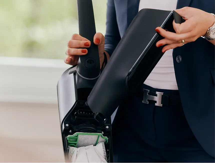 Eine Person öffnet ein schwarzes Haushaltsgerät und zeigt das Innenleben mit eingesetztem Staubbeutel.