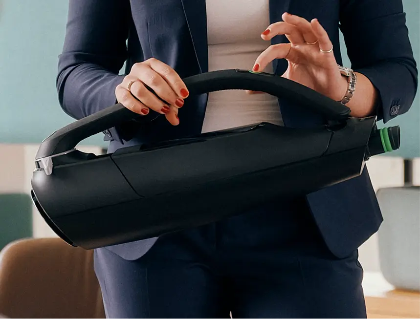 Eine Person hält einen schwarzen kabellosen Staubsauger am Griff und zeigt dessen Handhabung.