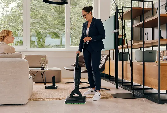 Eine Person demonstriert die Anwendung eines kabellosen Reinigungsgeräts im Wohnzimmer.