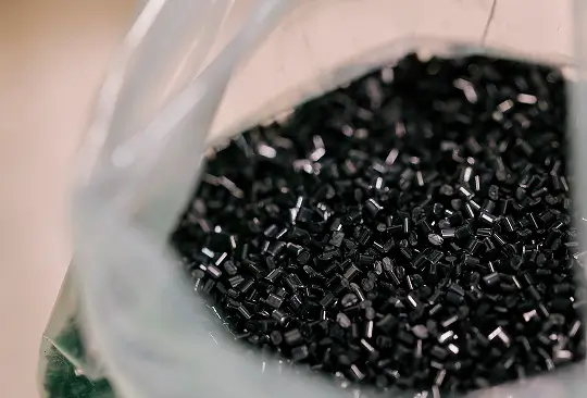 Schwarzes Kunststoffgranulat in weißem Behälter in Nahaufnahme.