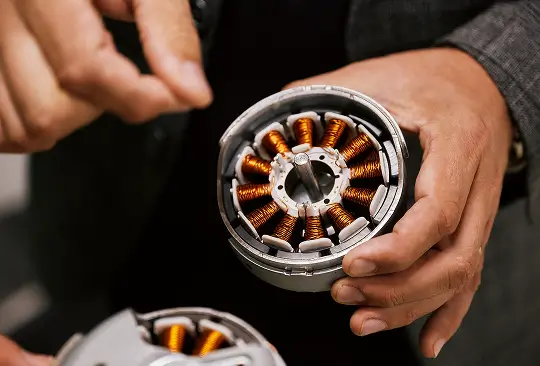 Hand hält einen Elektromotor mit sichtbaren Kupferspulen und silbernem Gehäuse