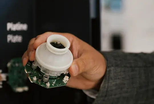 Hand hält eine runde Motor-Komponente mit Platine vor schwarzem Hintergrund mit Aufschrift