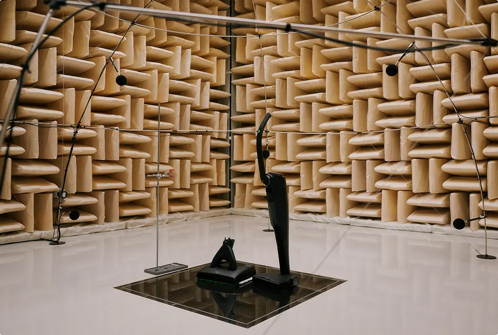 Schalldämmraum mit beigen Schaumstoffkeilen an Wänden und schwarzen Skulpturen auf Spiegelfläche.