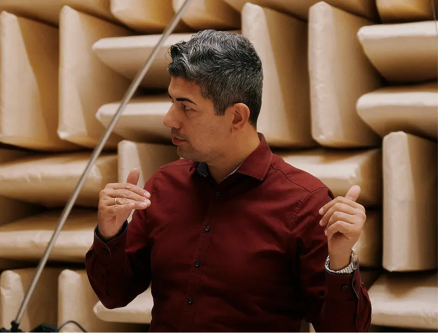 Mann im bordeauxfarbenen Hemd gestikuliert vor schallabsorbierenden Wandpaneelen