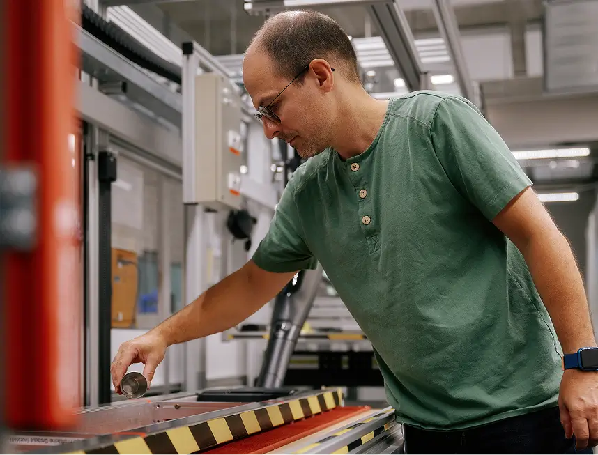 Mann in grünem T-Shirt prüft mit Metallzylinder eine Teststrecke in moderner Produktionshalle