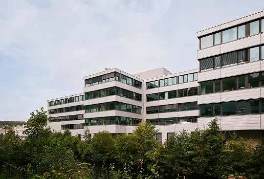 Moderne Bürogebäude mit großen Fenstern und umliegenden Bäumen unter bewölktem Himmel