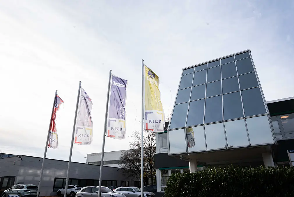 Ein Bürogebäude mit Glasfassade und Fahnen davor.