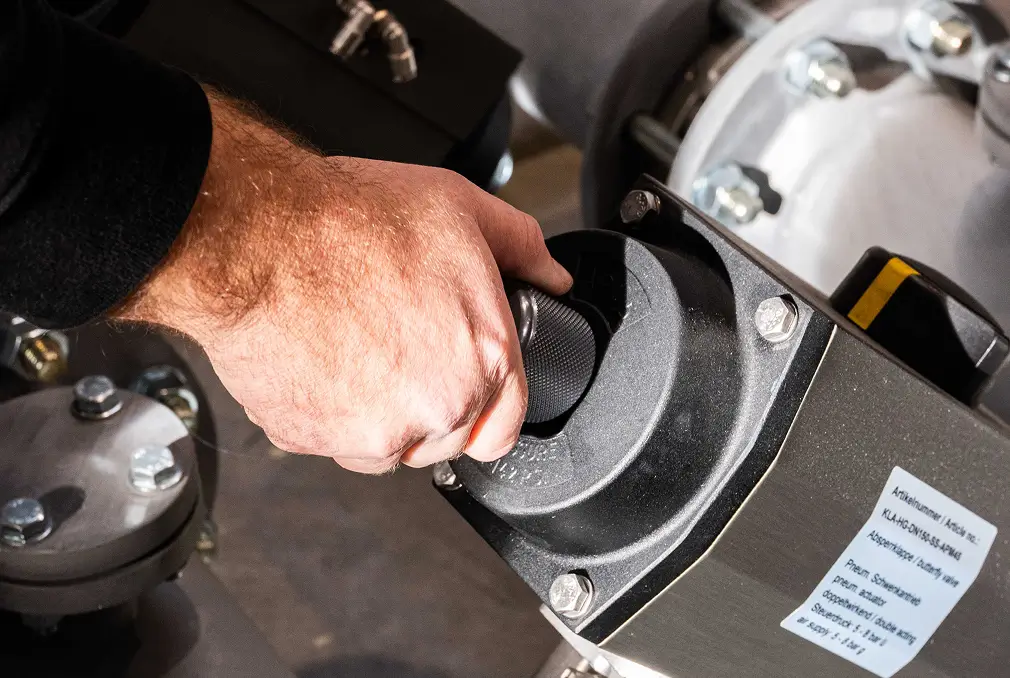 Hand dreht ein schwarzes Ventil an einer Maschine.