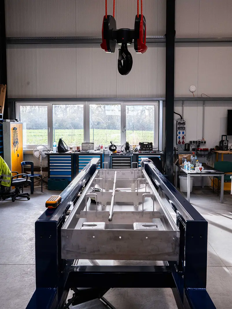 Ein Metall-Maschinenbett in einer Werkstatt, darüber ein roter Kranhaken.