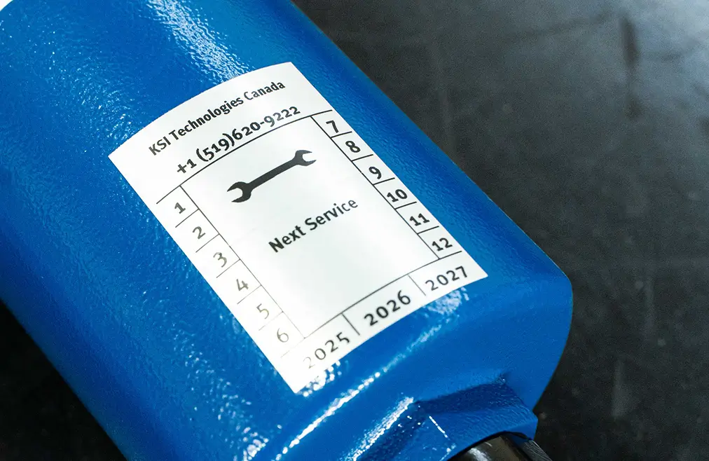 Nahaufnahme eines blauen Bauteils mit Wartungslabel und Schraubenschlüssel-Symbol.