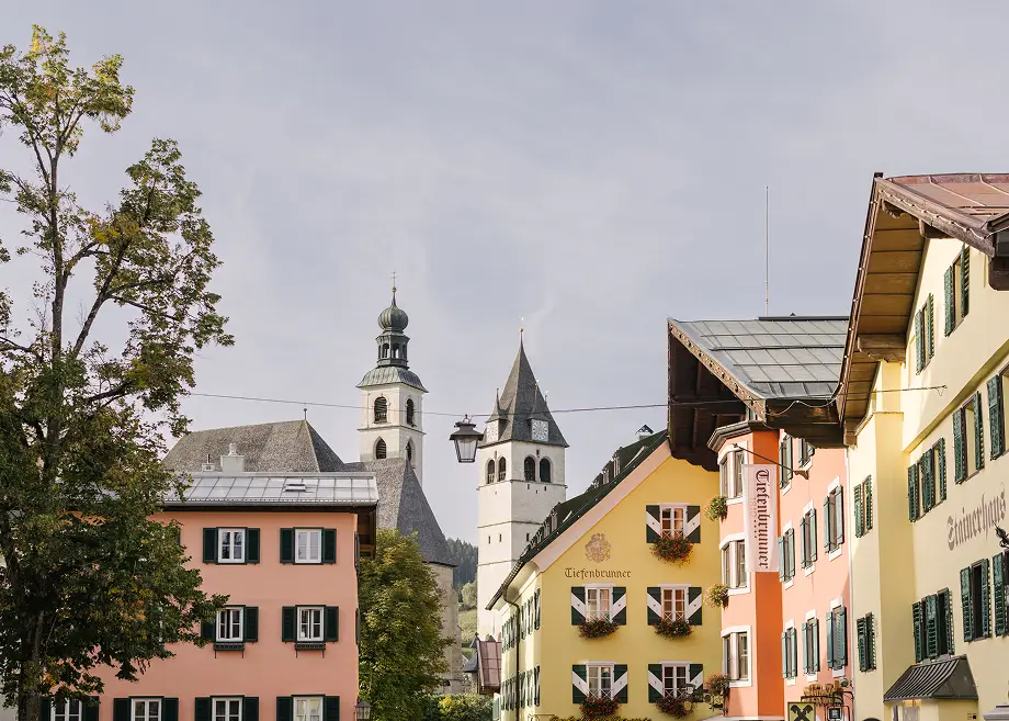 Blick auf pastellfarbene Häuser und Kirchtürme in der Altstadt von Kitzbühel unter hellem Himmel.