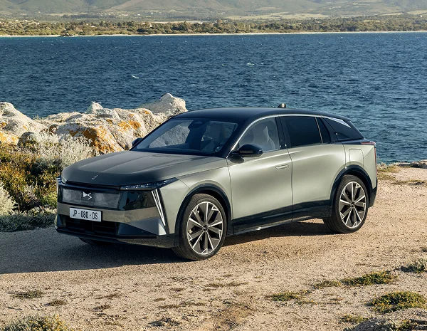 Grauer SUV steht auf einem felsigen Ufer an einem See, im Hintergrund sind bewaldete Hügel zu sehen.